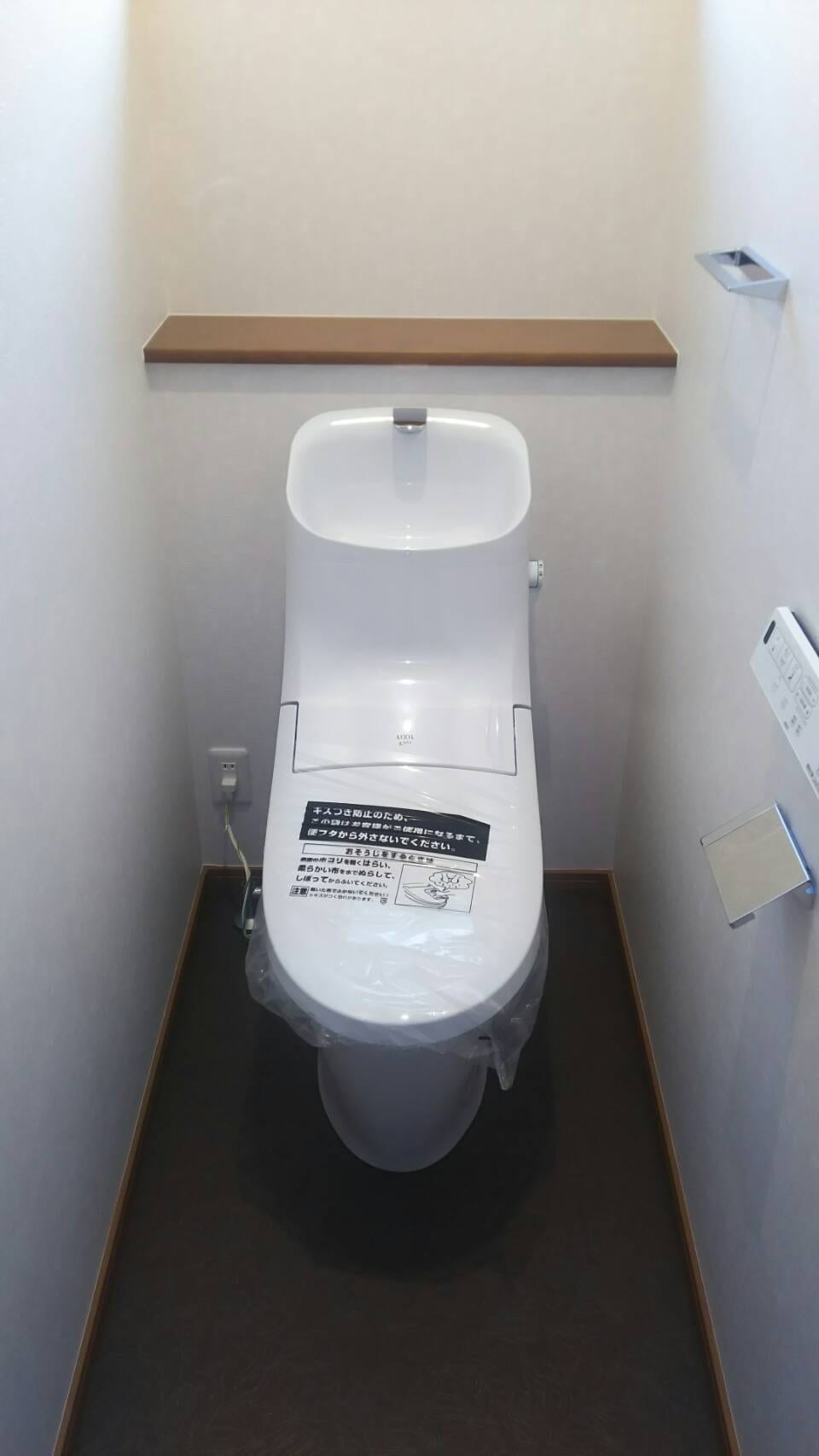淡いピンク系の壁紙と濃いブラウンの床を組み合わせたトイレ